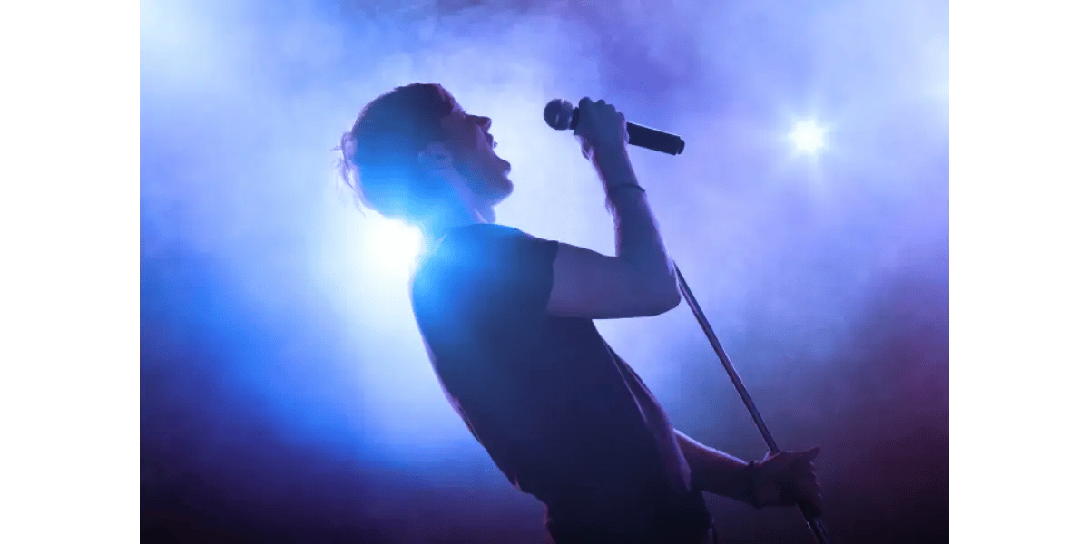 A singer performing vocal warm-ups and singing into a microphone on stage.