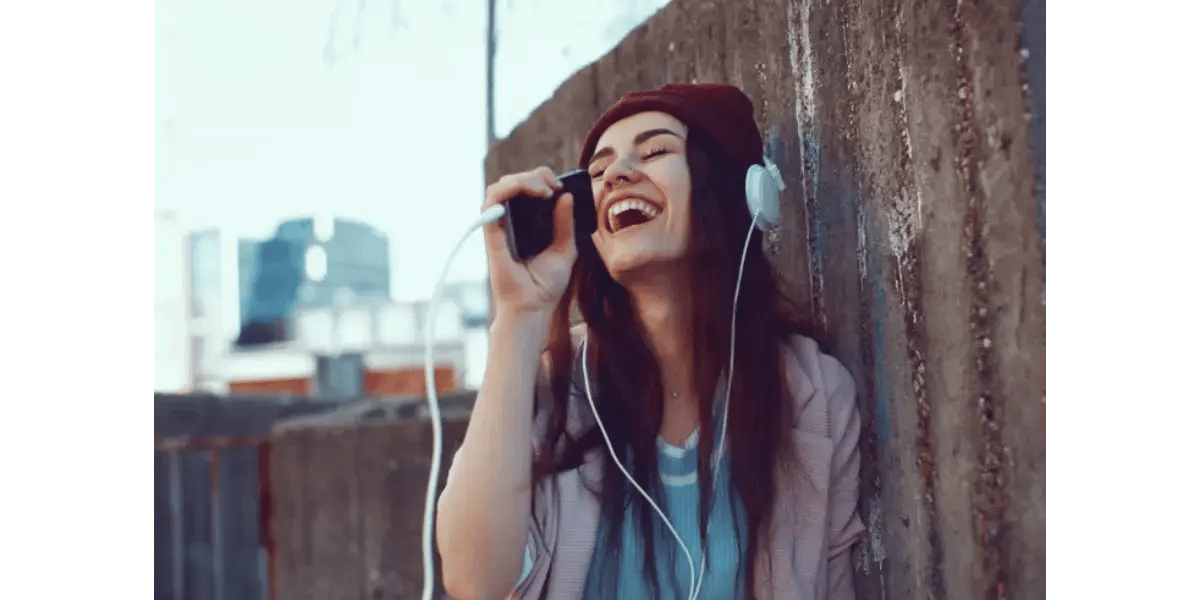 A smiling woman wearing a beanie and headphones outdoors.