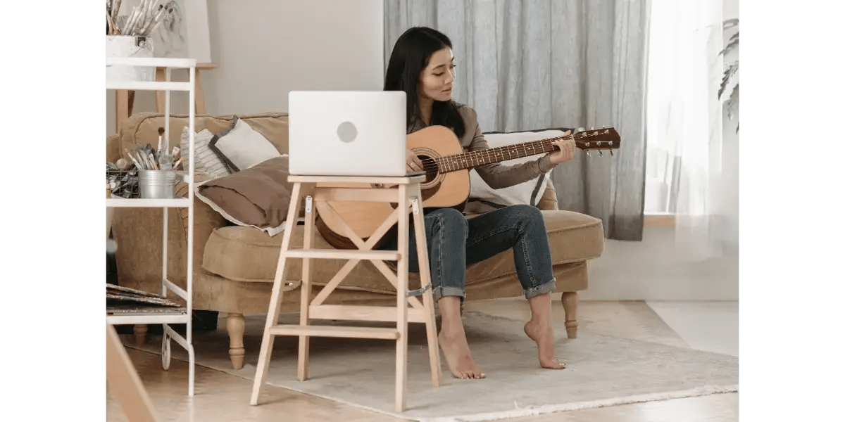 Woman working on a laptop in a home studio with a guitar.