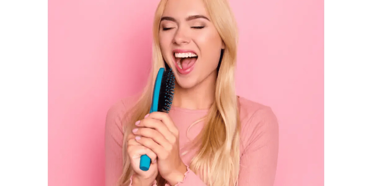 A woman playfully singing into a blue hairbrush, representing singing breath technique and airflow.