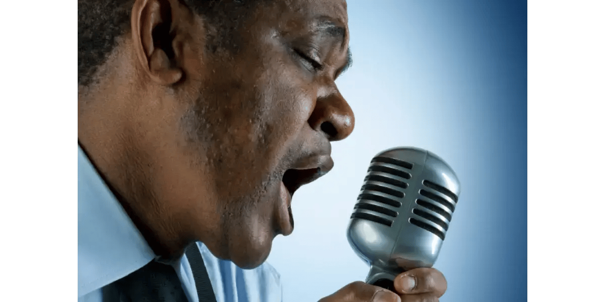 A singer demonstrating vocal energy and breath power while singing into a vintage microphone.