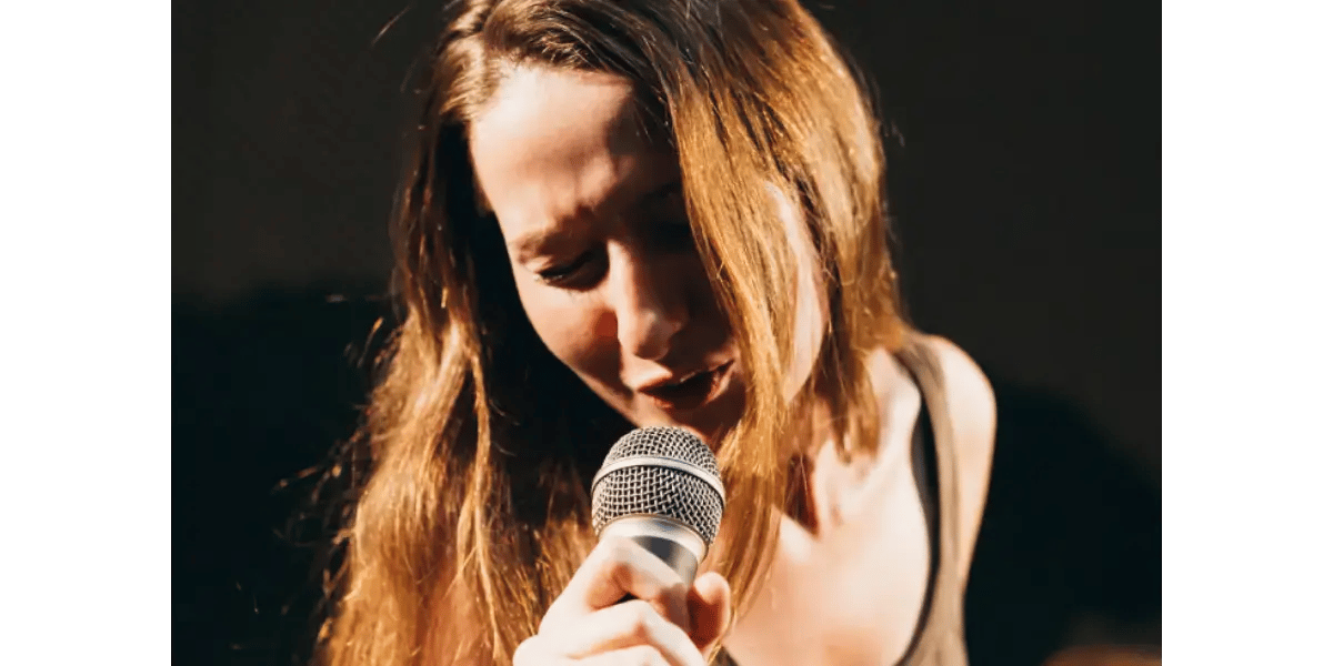 A close-up of a woman singing passionately into a microphone, representing relaxed breath support and how to avoid clavicular breathing.