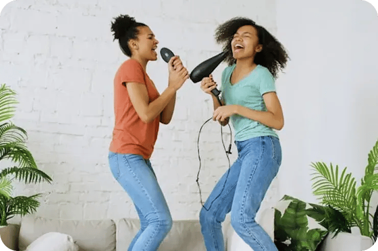 Two teenage girls singing enthusiastically together into a microphone during a teen voice lesson.