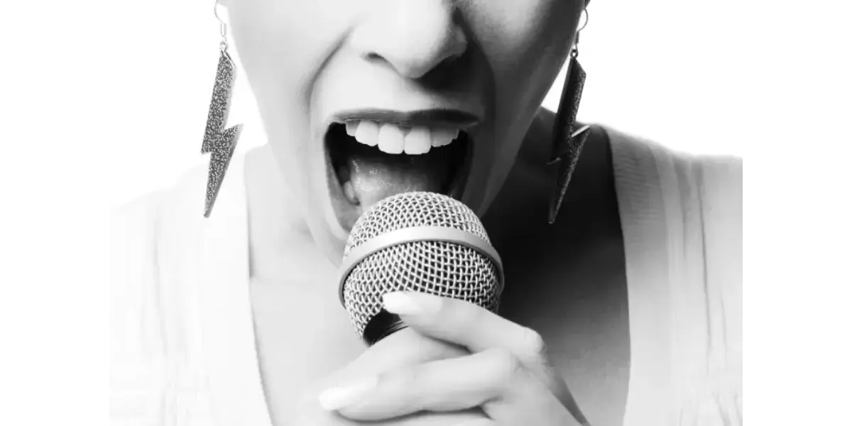 A black and white close-up of a person singing loudly into a microphone, representing chest-dominated registration and vocal volume.