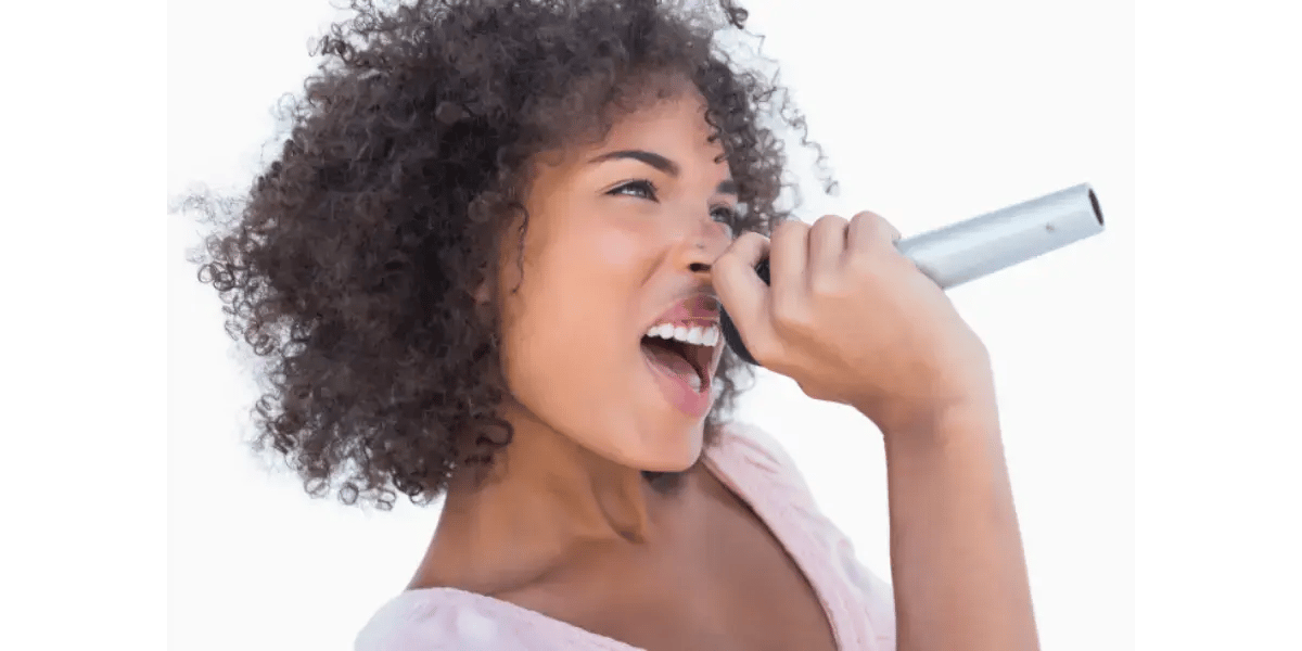 A close-up of a woman singing enthusiastically into a microphone, representing down and front vocal placement and tone resonance.