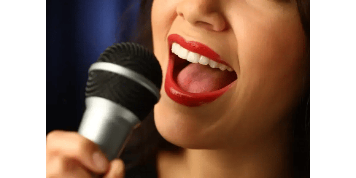 A close-up of a woman singing enthusiastically into a microphone, representing healthy vocal tension and muscle coordination.