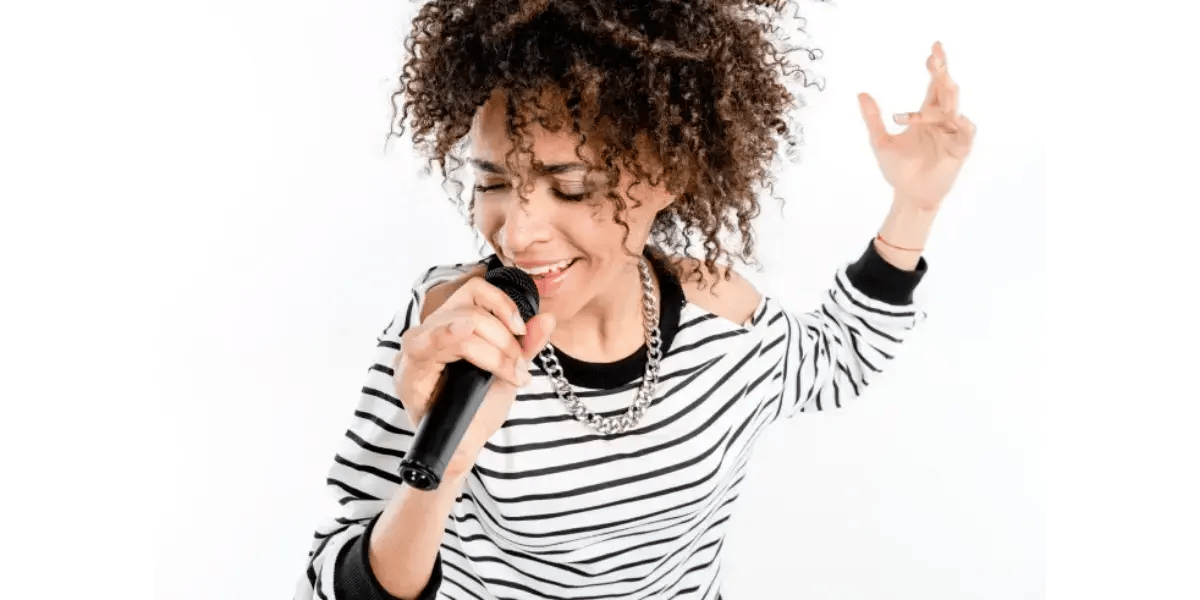 A female vocal student singing into a microphone, practicing chest voice registration and healthy vocal techniques.