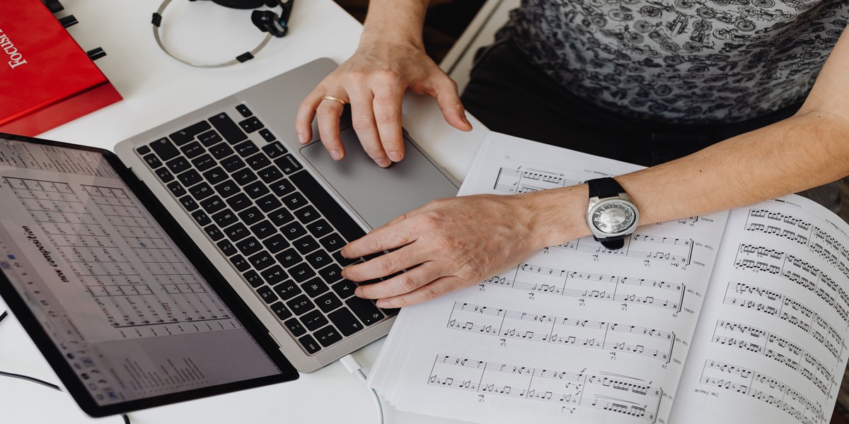 Close-up of hands typing on a laptop next to handwritten sheet music during an online lesson.