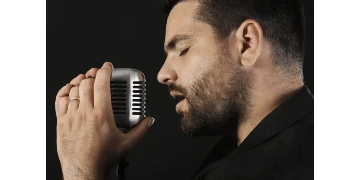 A male vocalist expressing deep emotion while singing into a studio microphone.