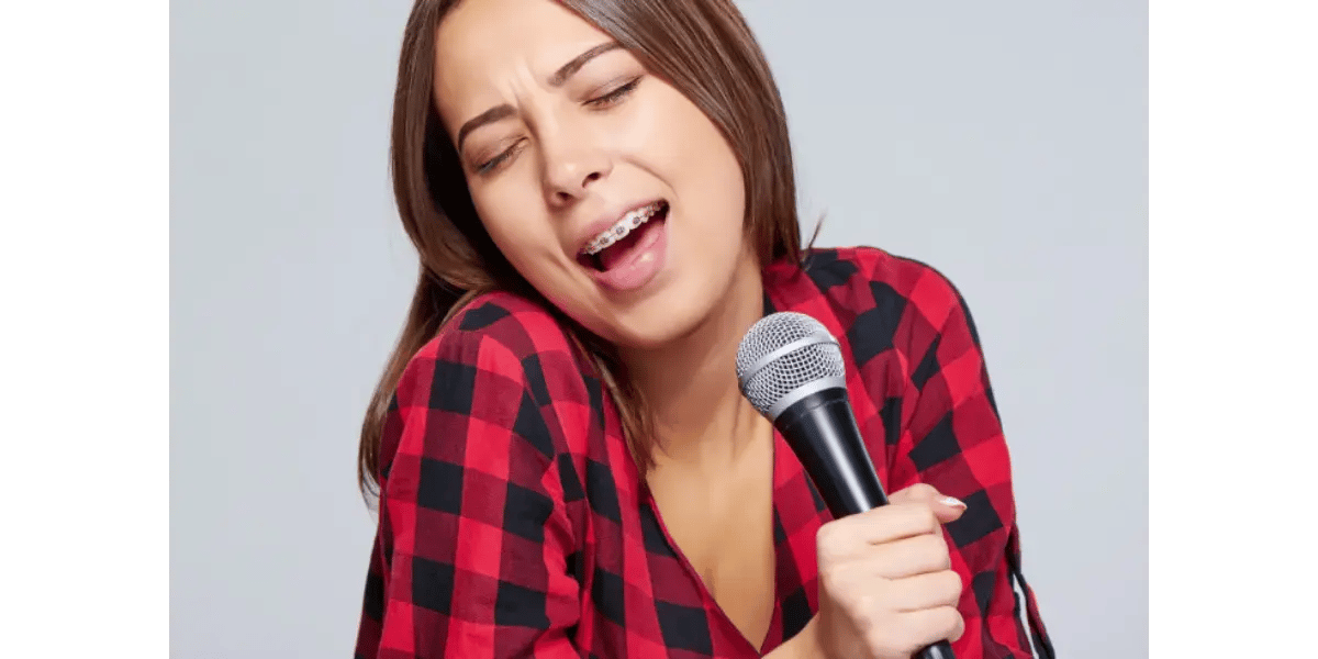 A singer demonstrating an open mouth position while performing into a microphone, representing vowel formation and vocal technique.