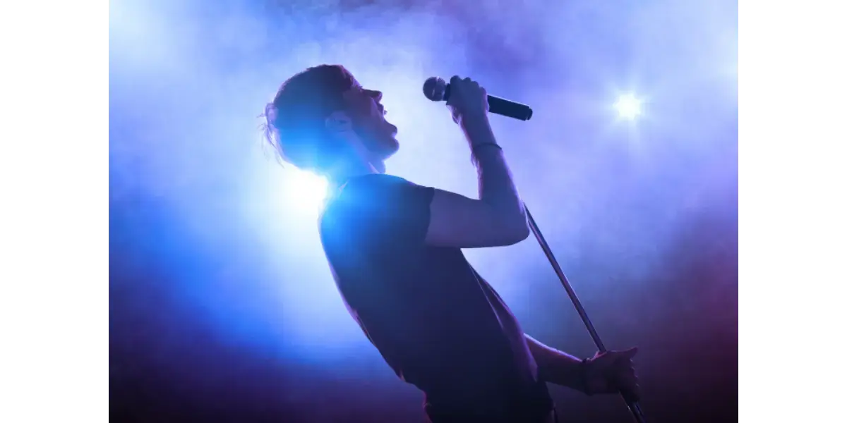 A singer performing vocal warm-ups and singing into a microphone on stage.