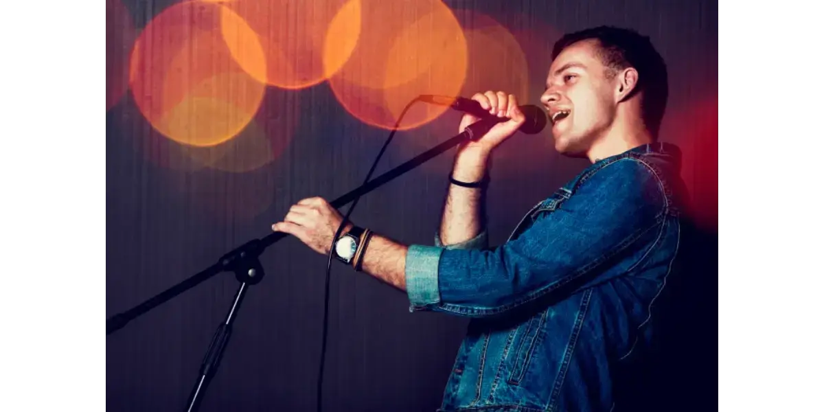 Male singer in a blue shirt performing live on stage with a microphone, representing vocal stretch and muscle balance.