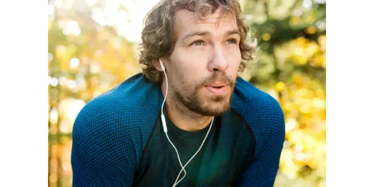 A man outdoors with earphones taking a breath, representing healthy breathing techniques and breath support for singers.