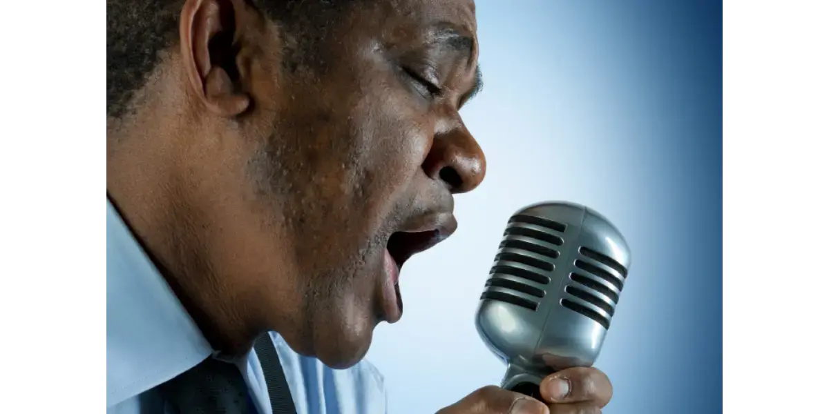 A singer demonstrating vocal energy and breath power while singing into a vintage microphone.