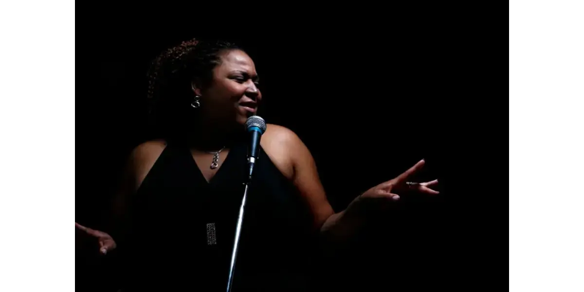 A singer performing passionately into a microphone on a dark stage, representing the power and control of a developed falsetto voice.