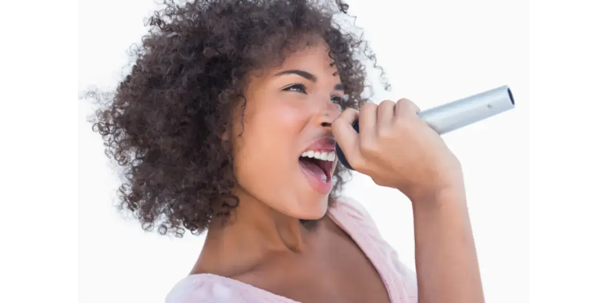 A close-up of a woman singing enthusiastically into a microphone, representing down and front vocal placement and tone resonance.