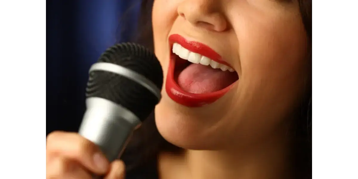 A close-up of a woman singing enthusiastically into a microphone, representing healthy vocal tension and muscle coordination.